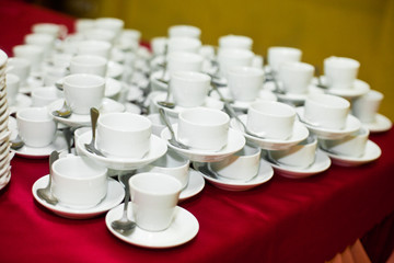 Empty white tea cups stand on the red tablecloth