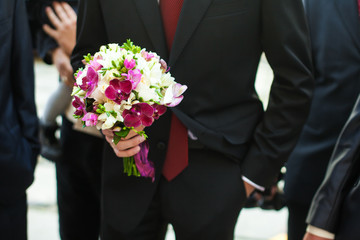 Groom in red tie holds violet wedding bouquet
