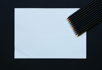 Blank paper and colorful pencils on black background