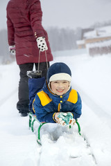 Fototapeta na wymiar Mom pulls a sled with his son on snowy road