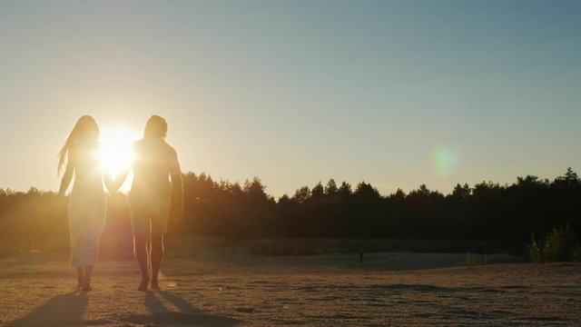 Steadicam shot: Silhouette of a young couple, which goes towards the setting sun. Back view