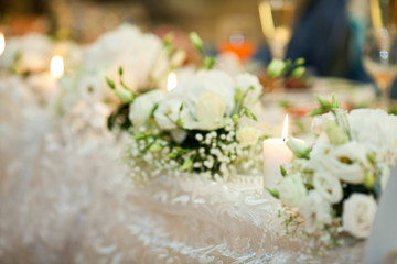 Burning white candles stand between white bouquets on the dinner
