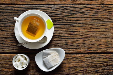 Top view of a cup of tea with tea bag and sugar cube on wooden table