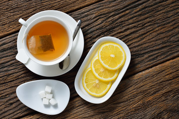 Top view of cup of tea with tea bag, sugar cube and lemon on wooden table