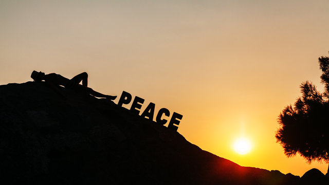 Man lying on the rock enjoying sunset with word peace written