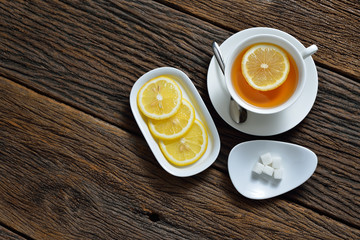 Top view of cup of tea with lemon and sugar cube on wooden table