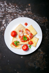 Homemade ravioli with tomato sauce, parsley and parmesan cheese on a white plate, top view