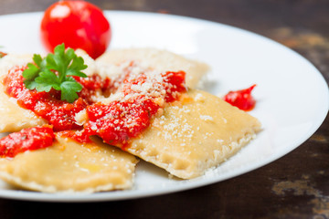 Homemade ravioli with tomato sauce, parsley and parmesan cheese on a white plate, closeup