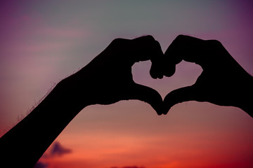 Fototapeta premium Love sign. Heart symbol by hand silhouette in sunset sky. Vintag