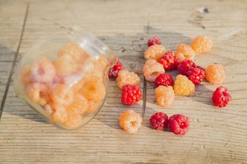 Multicolored raspberries in a glass jar on  old wooden background