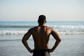 Back view of black fit sportsman looking the sea for motivation before swimming. Male swimmer ready...
