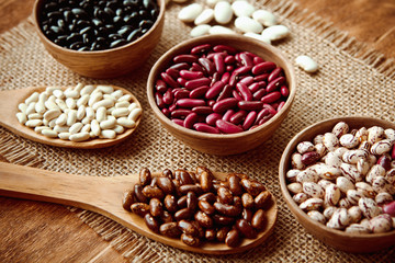 Beautiful multi-colored beans in bowls and wooden spoons on a background of burlap
