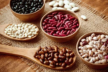 Abwaschbare Fototapete Beautiful multi-colored beans in bowls and wooden spoons on a background of burlap © mikhail_kayl