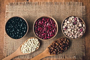 Beautiful multi-colored beans in bowls and wooden spoons on a background of burlap