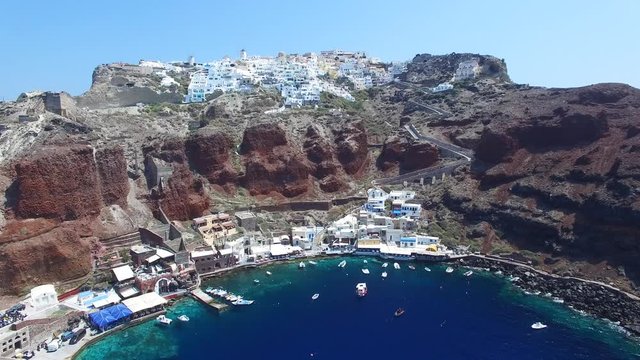 Aerial footage of Oia, Santorini - Famous white houses and blue domes on the edge of the cliff and blue lagoon.