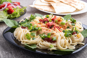 Closeup black plate with spaghetti and pieces of stewed chicken
