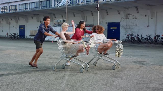 Young friends racing grocery carts. Multiracial group of young people enjoying outdoors with shopping trolley race.
