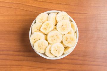 Banana slices into a bowl over a wooden table