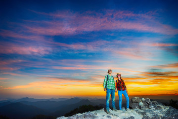 Two  happy hikers with backpacks enjoying sunset view from top of a mountain. Travel concept
