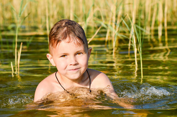 Fototapeta premium Boy swims in the lake water with a green tint.