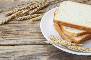 Sliced white bread on a plate with ears of wheat on a wooden tab