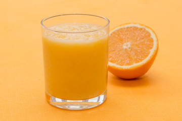 Orange smoothie in glass on orange background