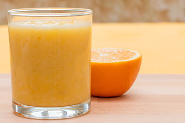 Orange smoothie in glass on orange background