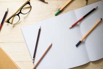 blank paper and colorful pencils and glasses on old wooden table with mornning light.