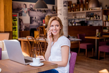 Woman in cafe, talking on phone, working on notebook