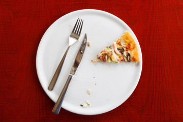 one slice of pizza on a white plate. Wooden table, knife and fork.