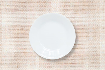 Closeup white ceramic dish on brown fabric mat textured background at the center on dining table in top view with copy space