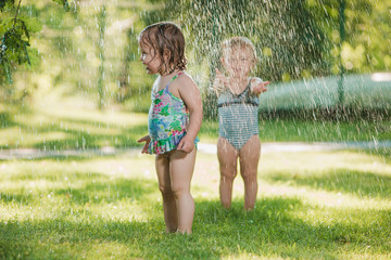 The two little baby girls playing with garden sprinkler.