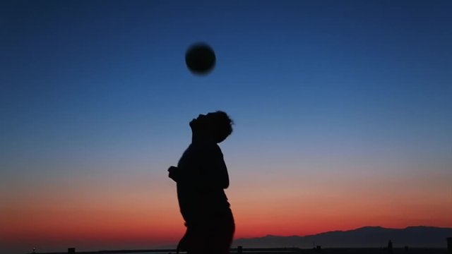 Cool slow motion of silhouette of man hitting soccer ball with head during sunset at beach