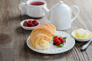 Fresh croissant with raspberry and tea for breakfast on dark wooden table