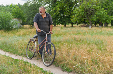 Obraz premium Senior peasant standing on a country road with old rusty bicycle and dream about Grand Tour would ride through his village