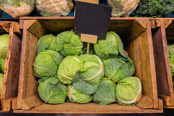 Fresh cabbage vegetable in wooden box stall in greengrocery with blank chalkboard label.