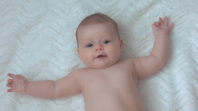 A cute little baby is looking into the camera and is happy on a white bed sheet.