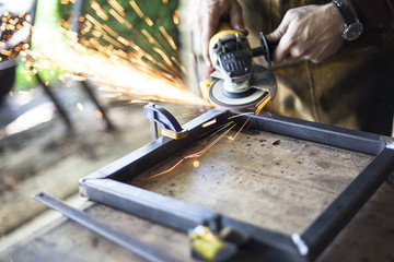 Custom furniture worker grinds weld seam on steel frame.