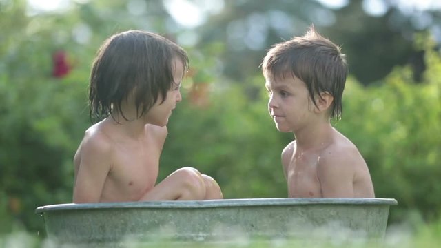 Two children, boy brothers, having a bath outdoors, making soap bubbles, summertime