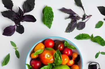 Multicolored tomatoes on a plate with basil leaves on top