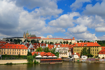 Obraz premium The Prague Castle, gothic style, largest ancient castle in the world and Charles Bridge, built in medieval times, moving boats, Summer view of Prague with blue sky with big white clouds. River Vltava.