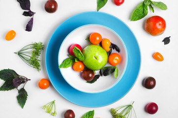 Multicolored tomatoes on a plate with basil leaves on top