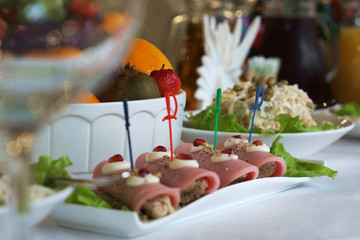 Appetizer of rolls with ham on the holiday table. Cold appetizers Banquet dinner served. Festive feast and food.