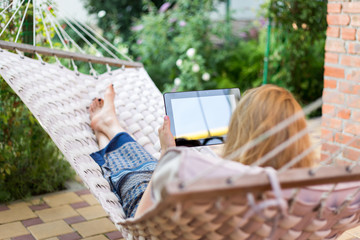 Woman using tablet computer while relaxing in a hammock