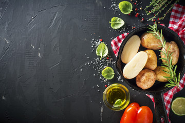 Young ripe potatoes in a black cast iron pan with herbs, olive oil, rosemary, pepper, sea salt for baking. Healthy homemade food, Vegetarian and diet. Top view