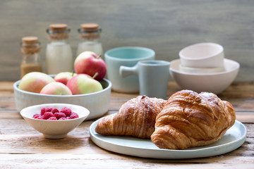 Delicious breakfast with fresh croissants, raspberries, apples and milk on old wooden background