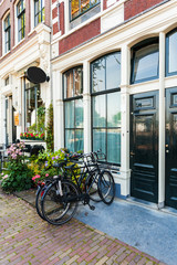 Fototapeta na wymiar Fragment of colorful typical dutch building in Amsterdam with bicycles, standing near the entrance to the house and flowers in pots, Netherlands.