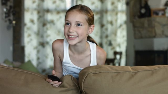 Child watching TV, little girl having fun on the couch, holding remote control
