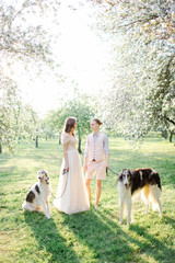 Naklejka na ściany i meble Beautiful young couple in wedding dress with greyhounds in park
