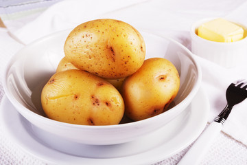 Boiled jacket potatoes served in a white bowl with butter